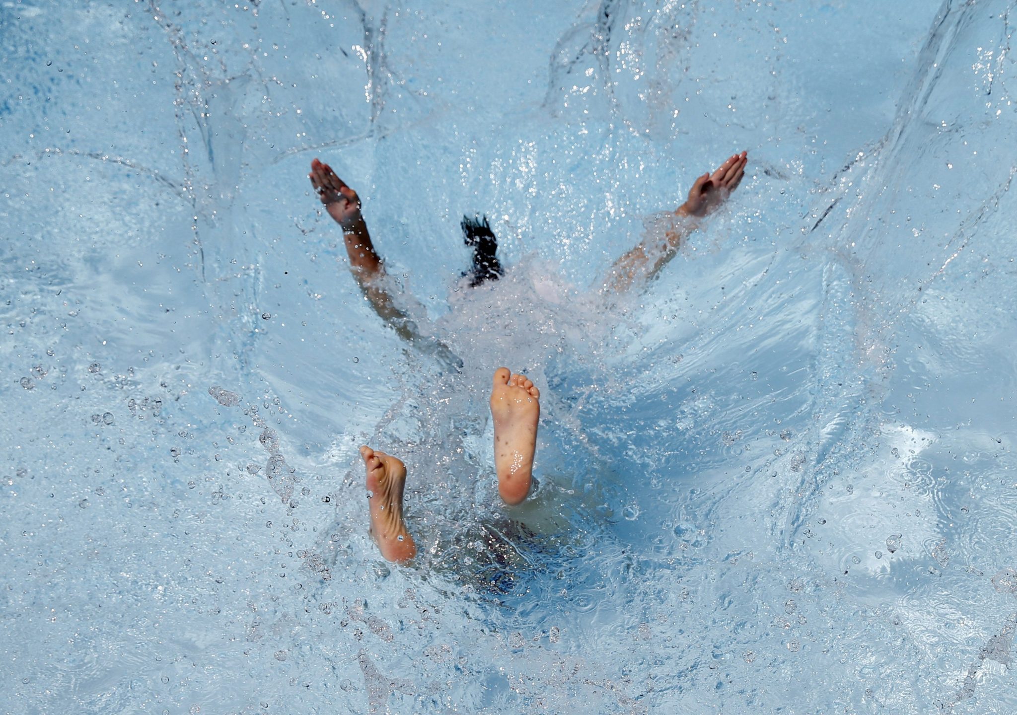 una niña se tira a una piscina para aliviar el calor.